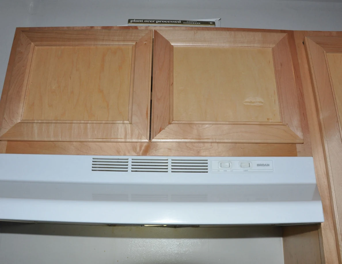 Closed wooden cabinet above a white range hood.