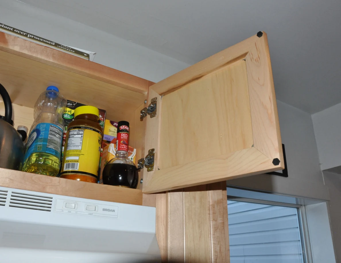 Angled view of open upper cabinet holding bottles, jars and a kettle.
