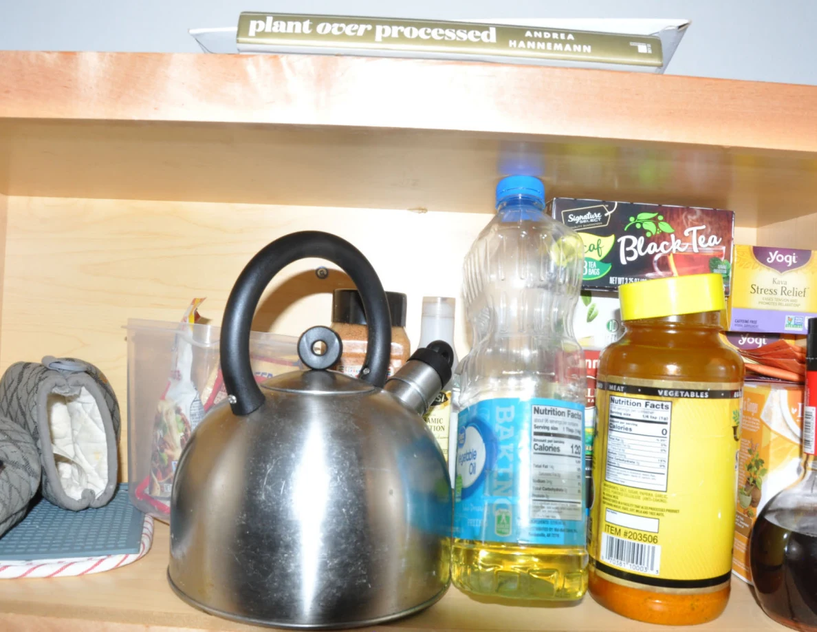 Close view of a metal kettle beside cooking oil, jars and tea boxes.