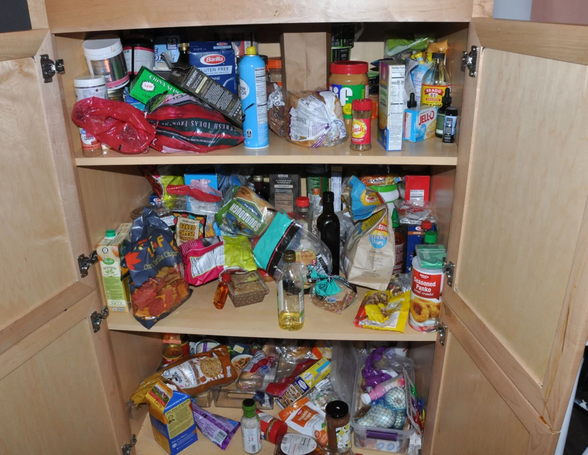 Open pantry cabinet filled with pasta, chips, spices, bottles and other groceries.