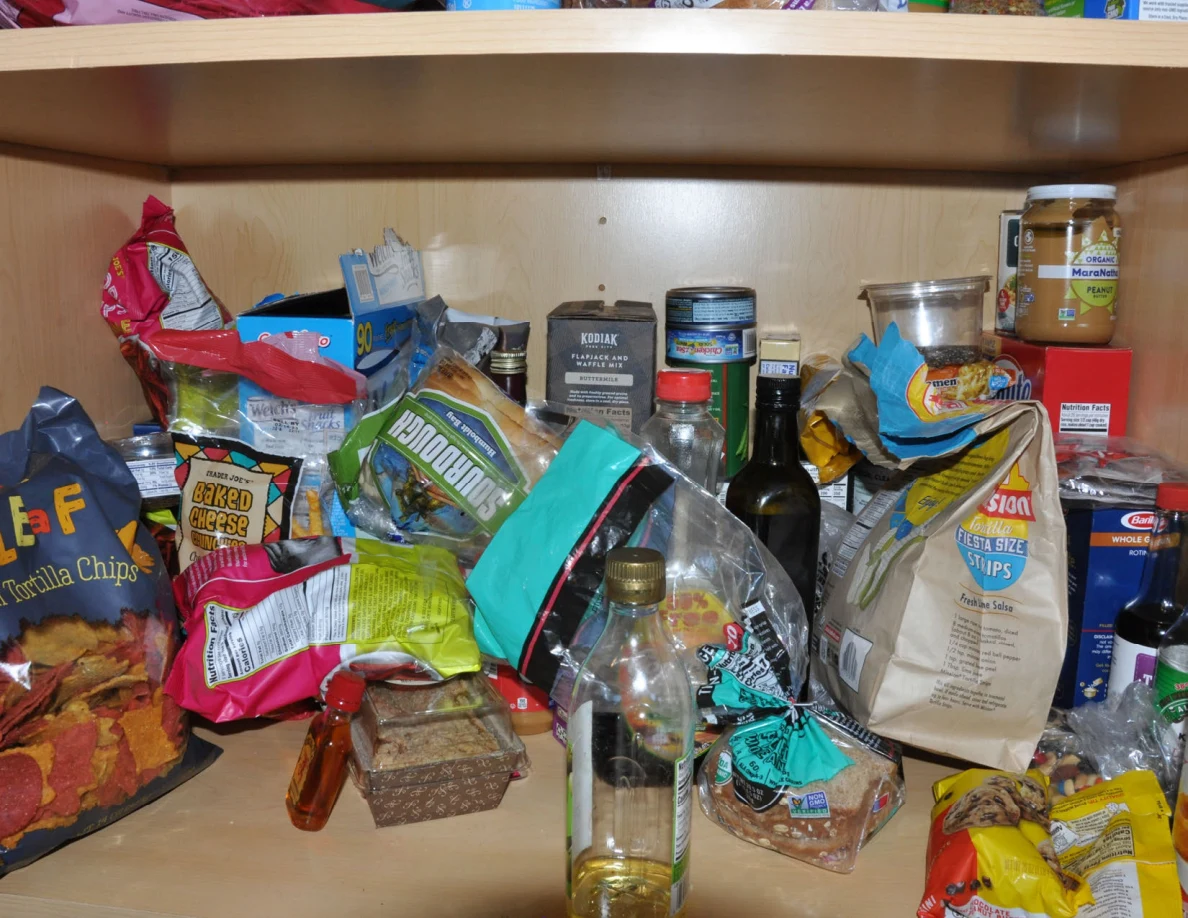 Pantry shelf packed with snack bags, bottles, jars and dry food packages.