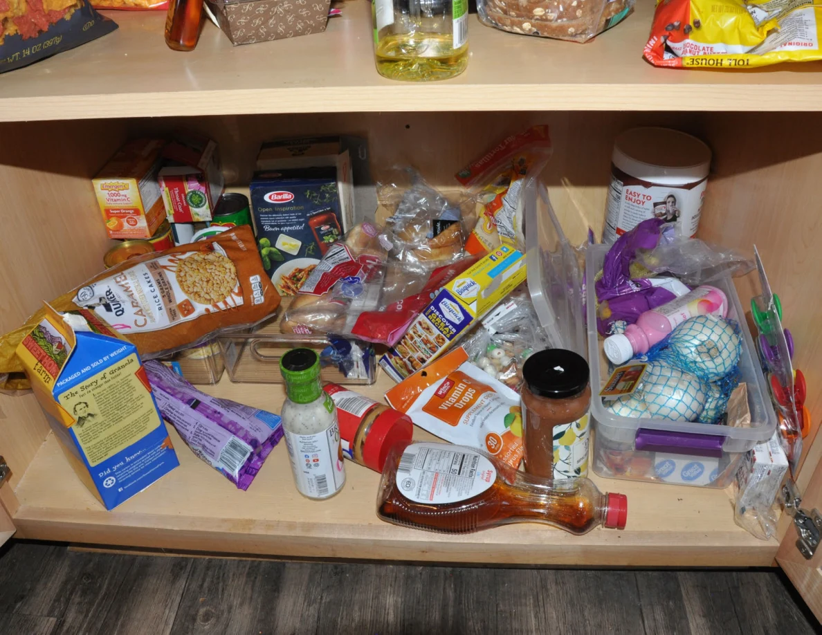 Lower pantry shelf containing assorted boxes, bottles, bags and storage bins.