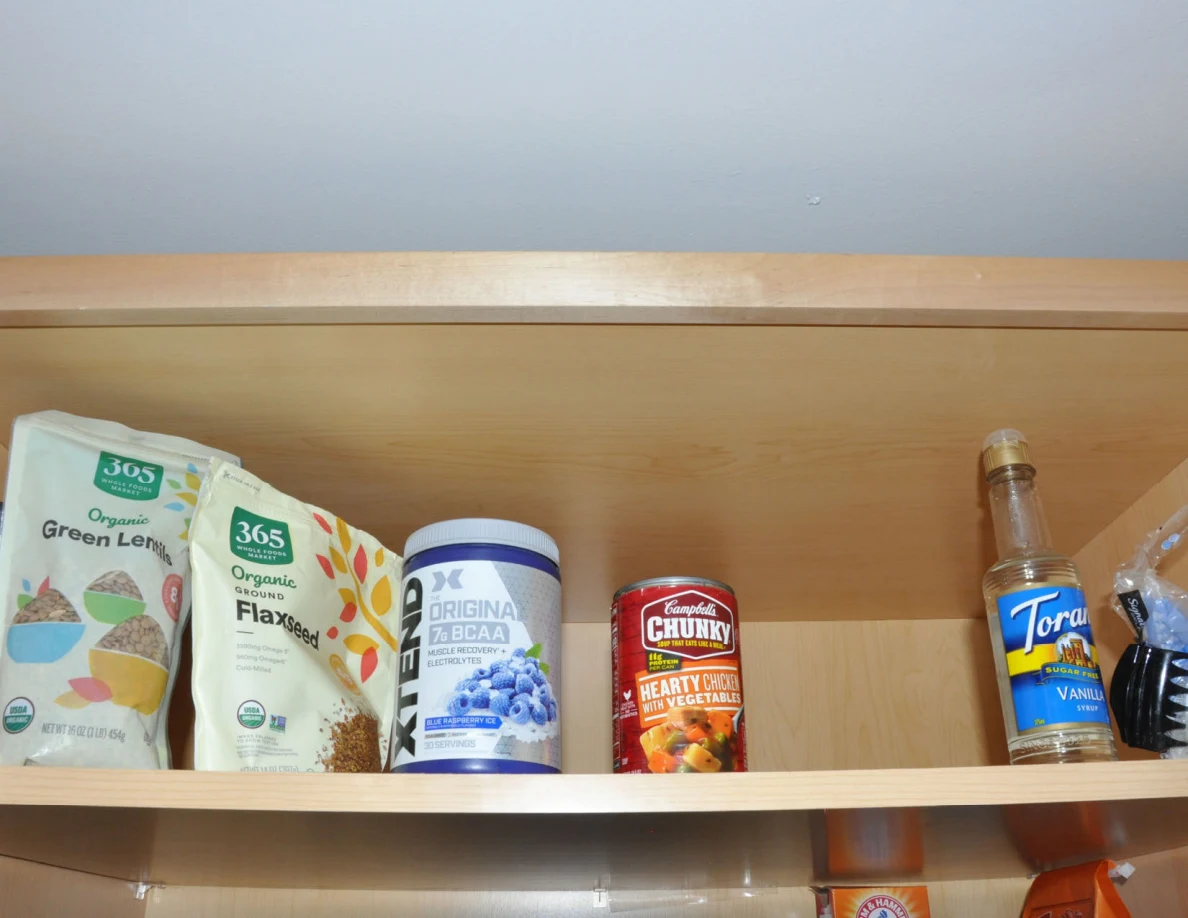 Upper pantry shelf with lentils, flaxseed, drink powder, canned soup and syrup.