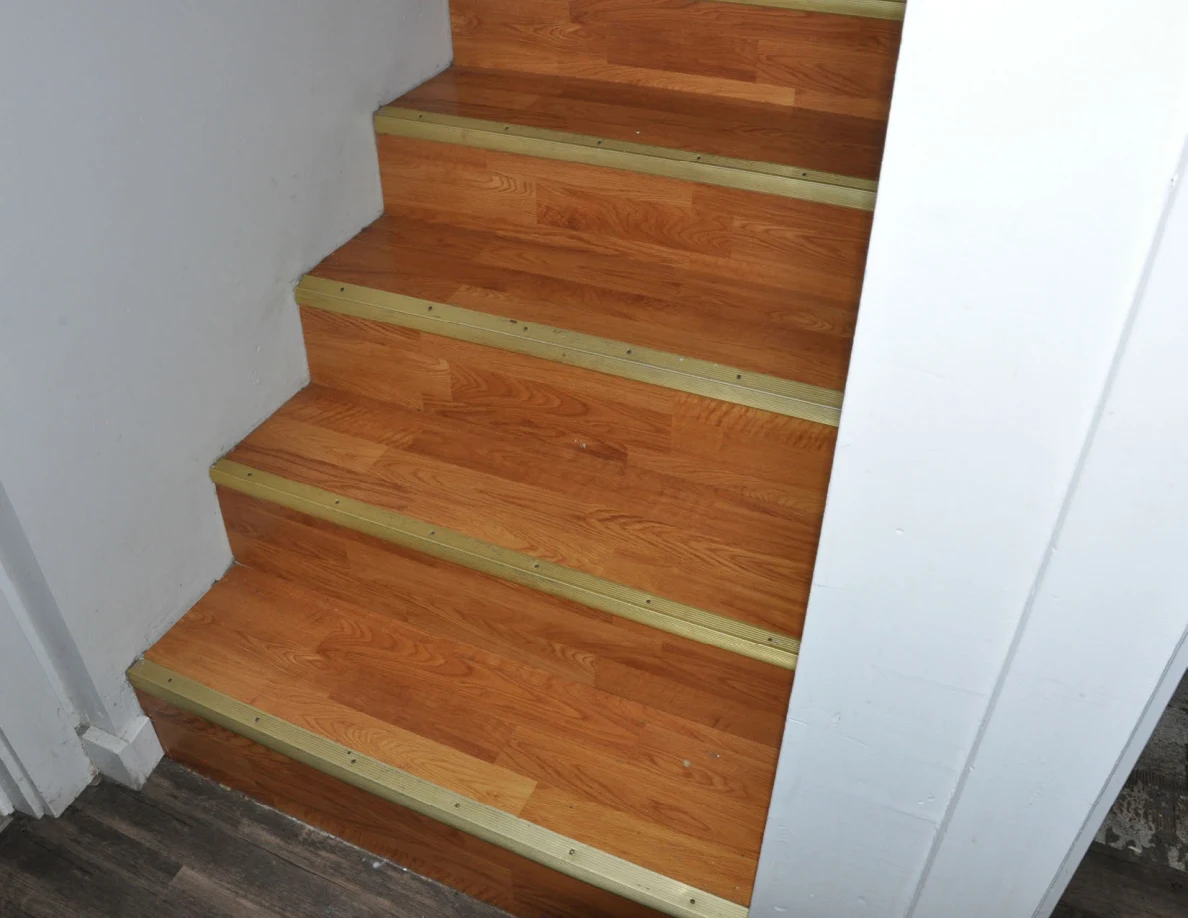 Lower wooden staircase with gold-colored step edges beside a white wall.