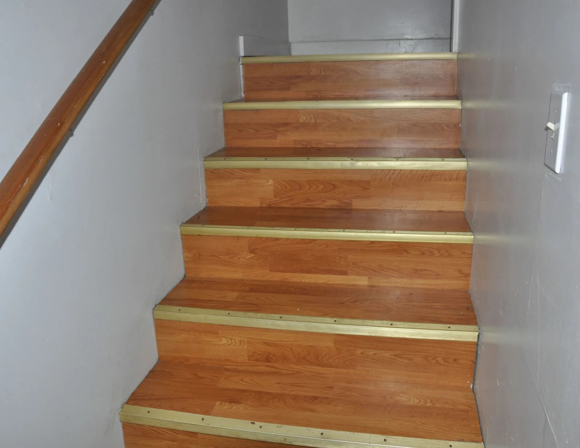 Wooden stairs ascending beside a handrail and wall light switch.