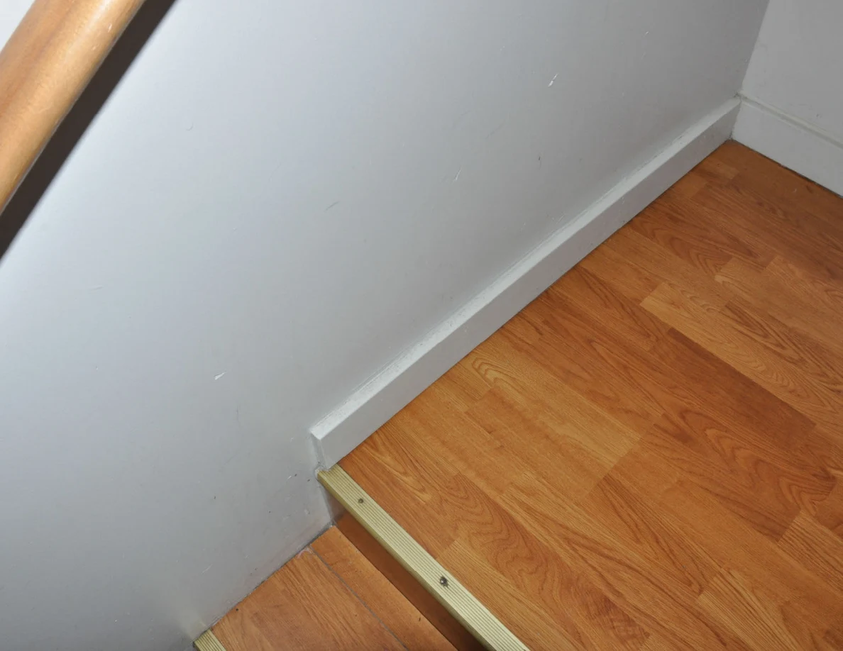 Wooden stair landing beside a white baseboard and wall.