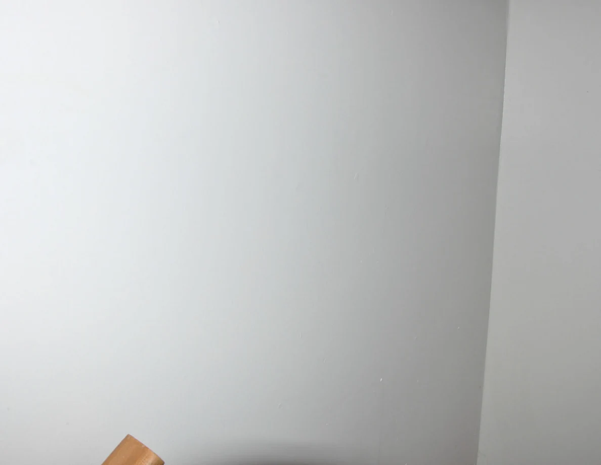 Plain white stairwell wall with the end of a wooden handrail at the bottom.