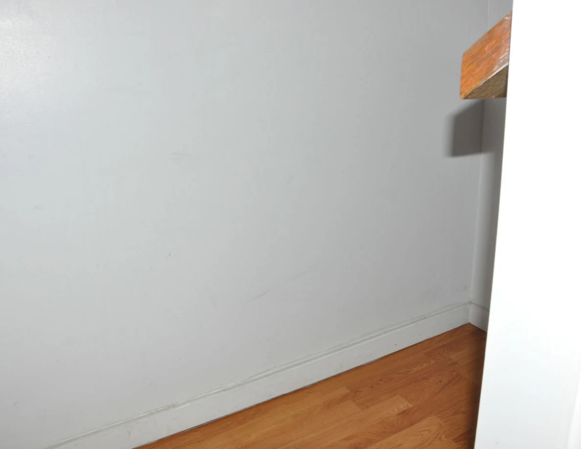 White stairwell wall above wood flooring beside a wooden rail cap.