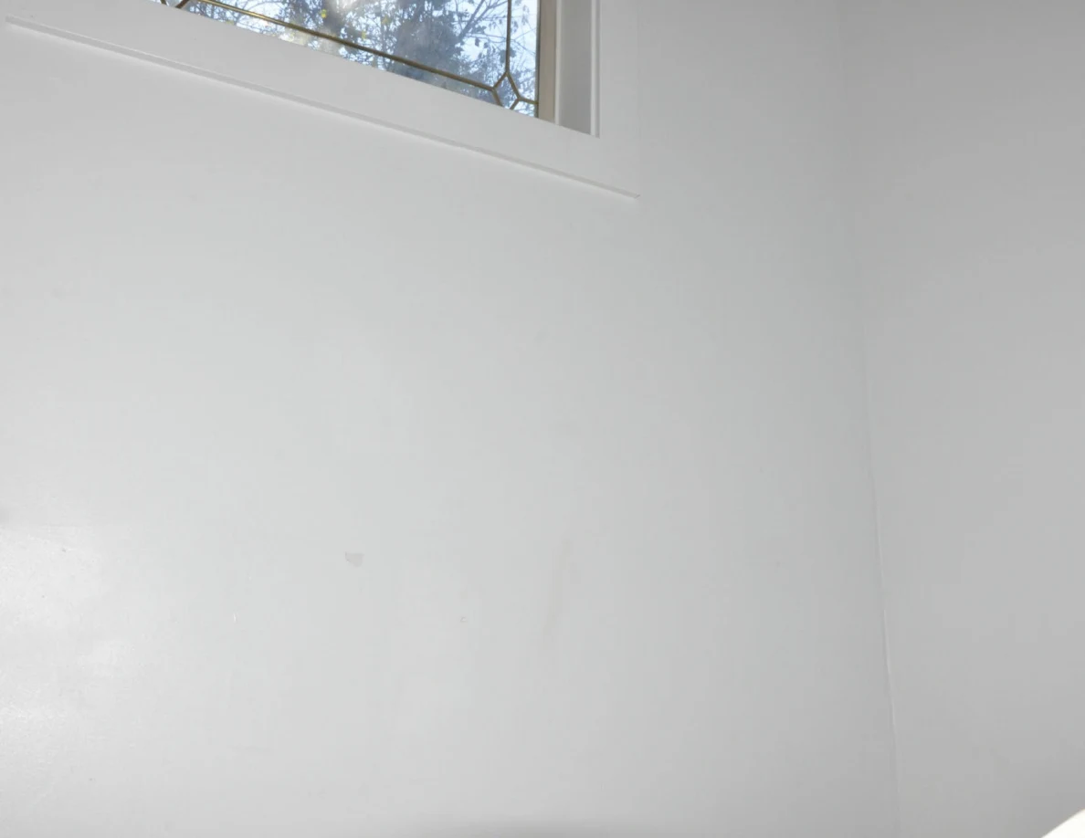 White stairwell wall beneath a high window.