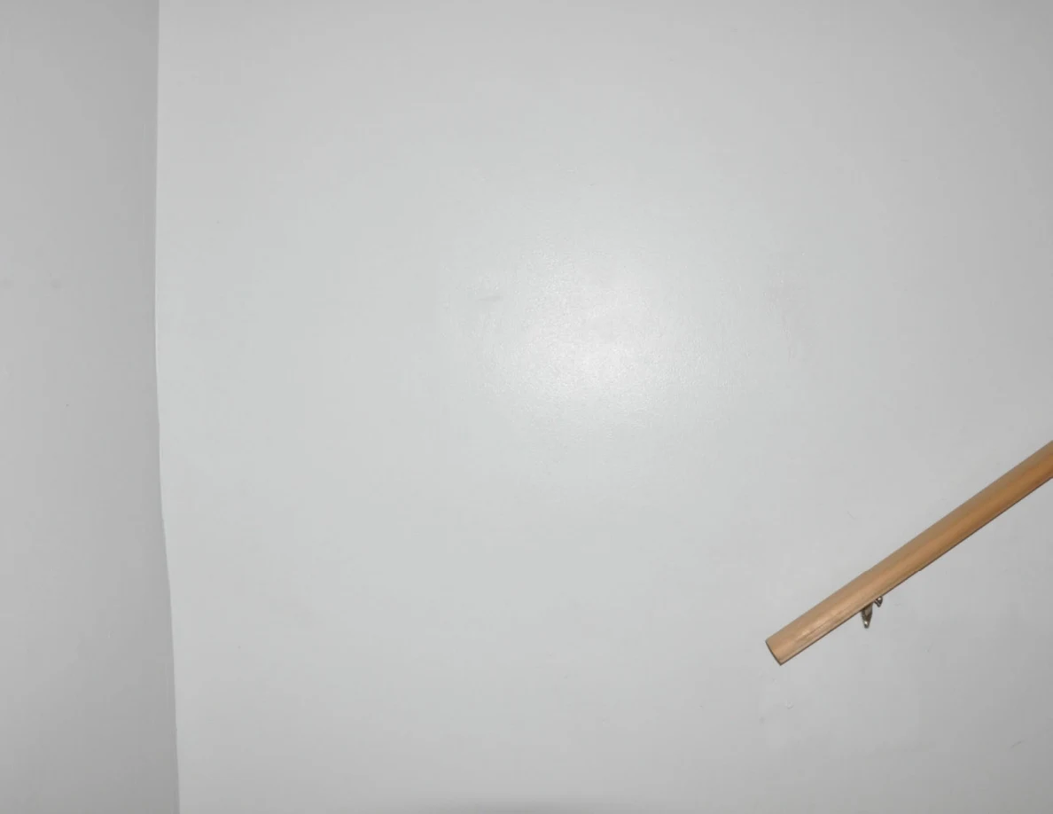 Plain white wall beside the end of a wooden handrail.