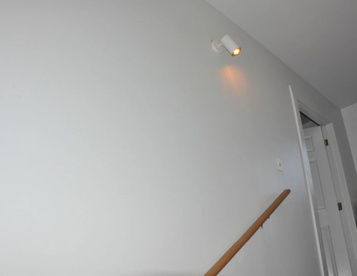 Wall-mounted light above a stair handrail near an open doorway.