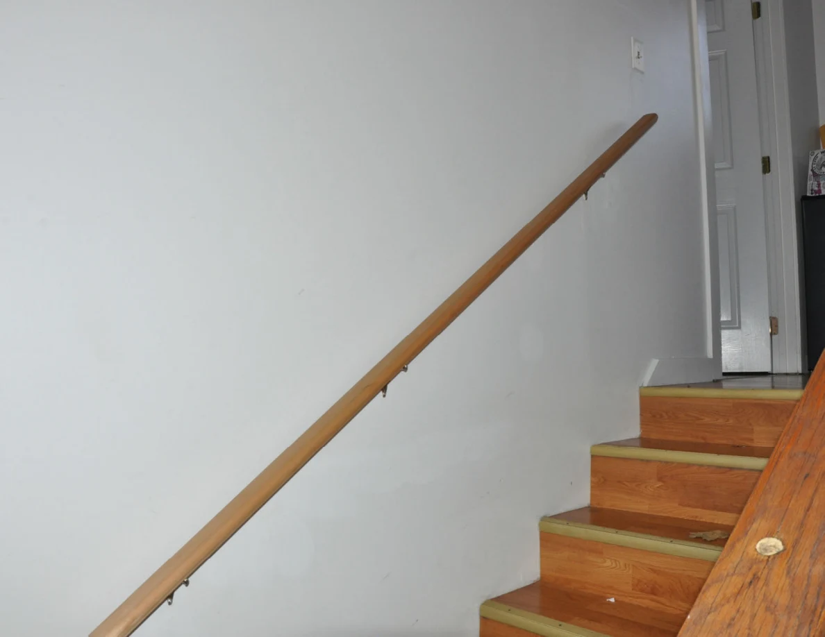 Wooden handrail beside upper stairs leading to an open white door.