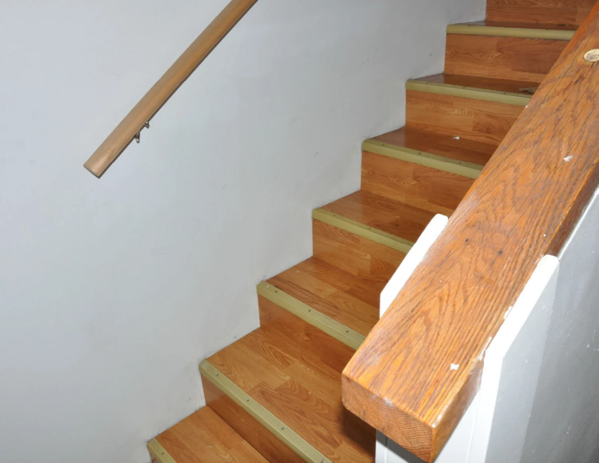 Angled staircase view with wooden handrail and broad rail cap.