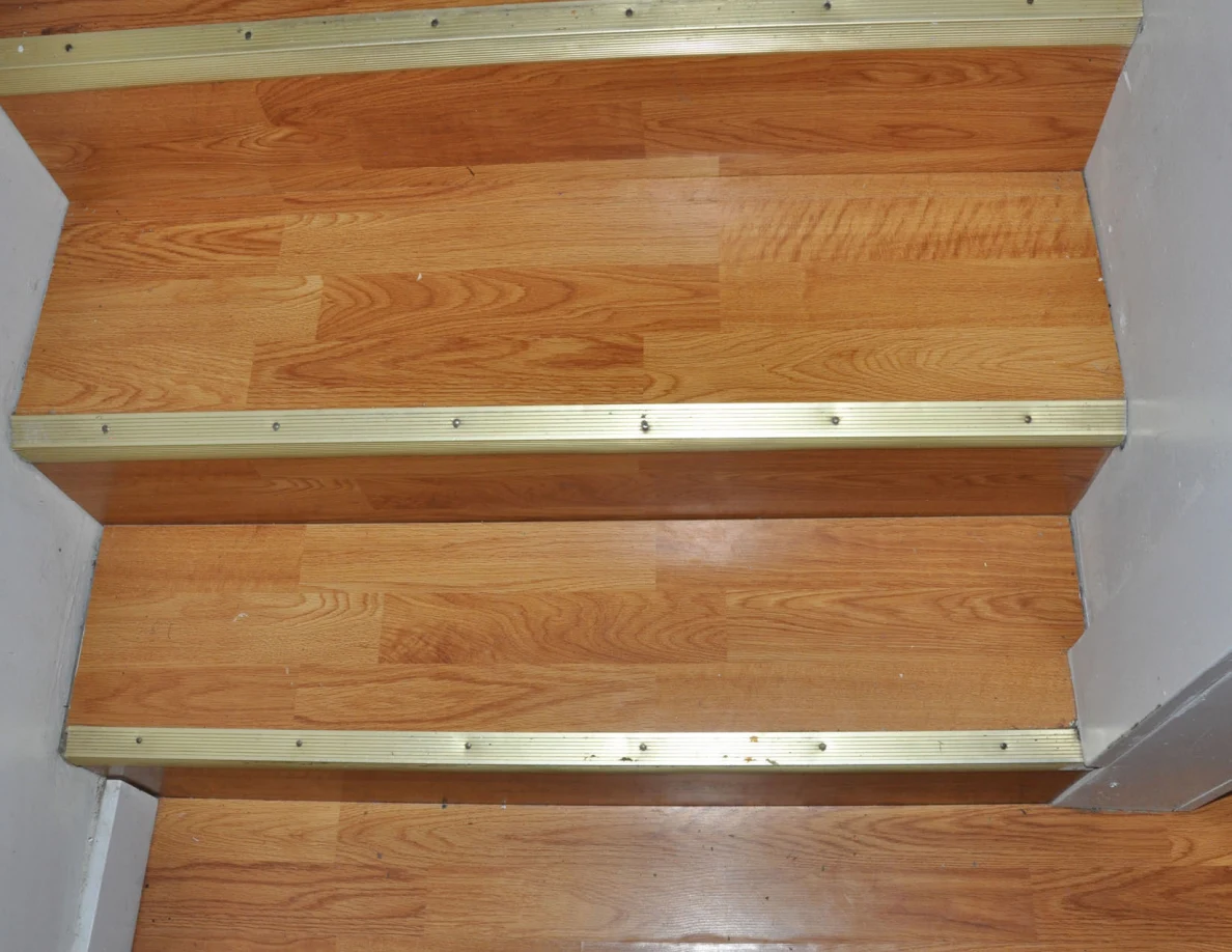 Close view of wooden stair treads with gold-colored metal edges.