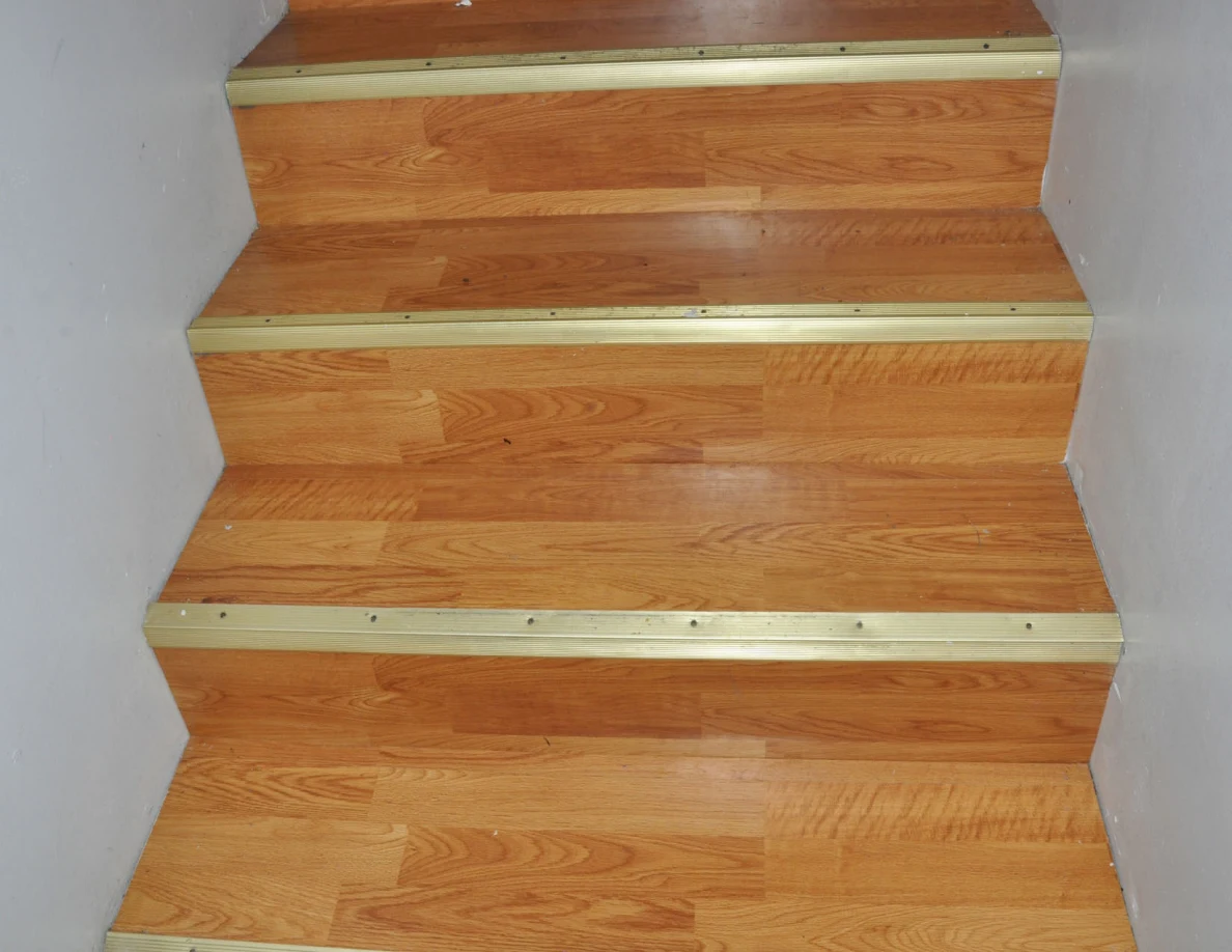 Wooden stair treads framed by white walls and gold-colored edge strips.
