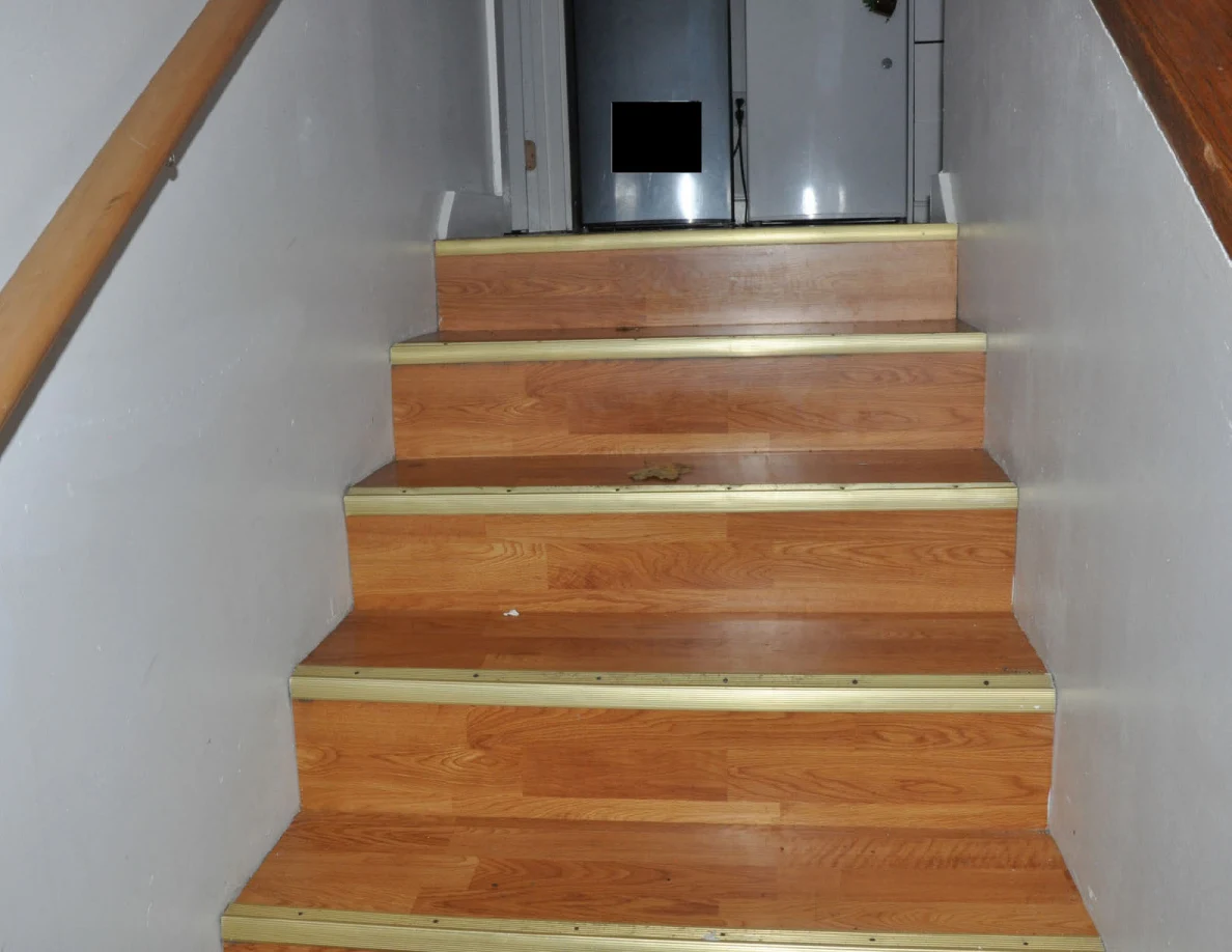 Upper wooden staircase leading toward compact refrigerators on a landing.