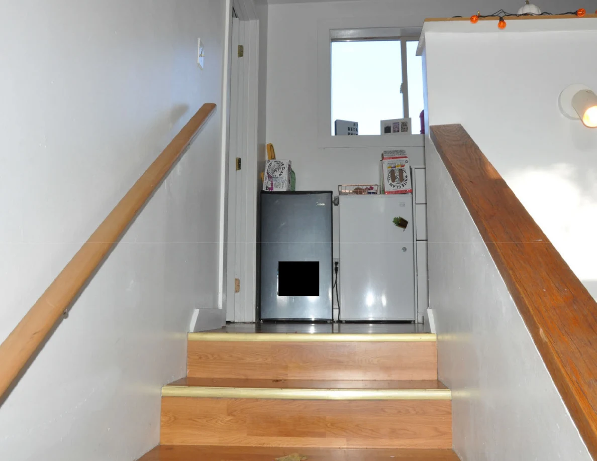 Stairs opening onto a landing with compact refrigerators beneath a window.