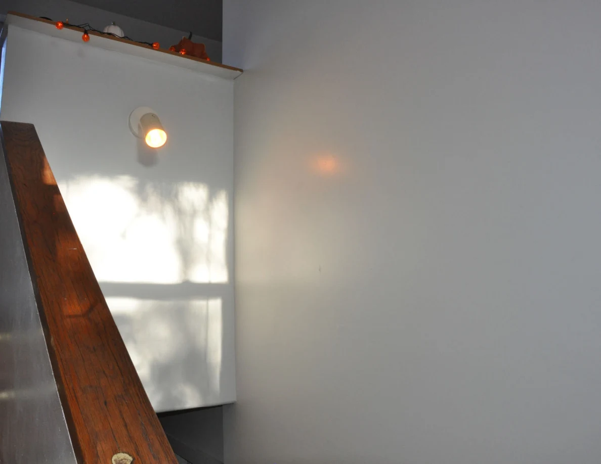 Stair half-wall with wooden cap, orange string lights and a wall-mounted lamp.