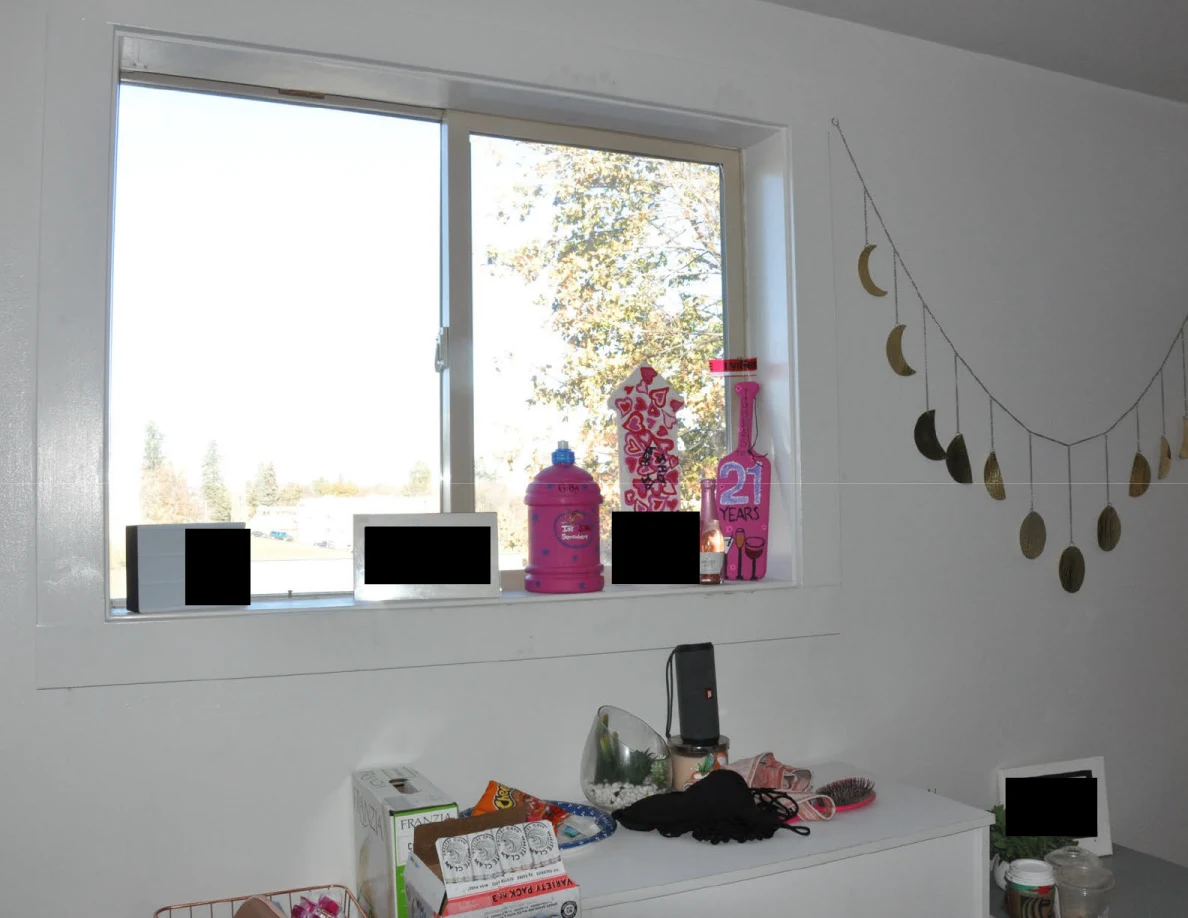 Window with decorative bottles and redacted items above drawers and a moon-phase garland.