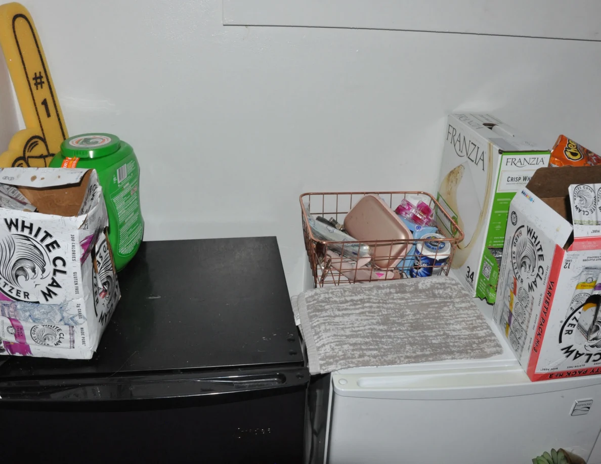 Tops of compact refrigerators holding drink cartons and a wire basket beneath a window.