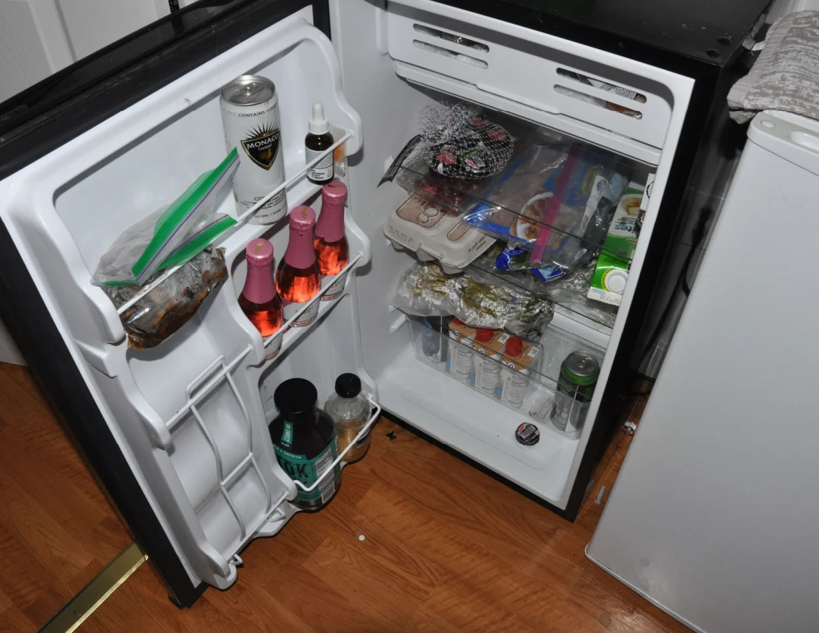 Open black mini refrigerator filled with bottles, cans, jars and food containers.