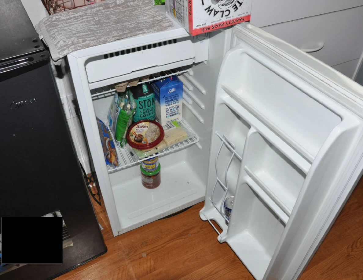 Open white mini refrigerator with drink cartons, bottles and food tubs.
