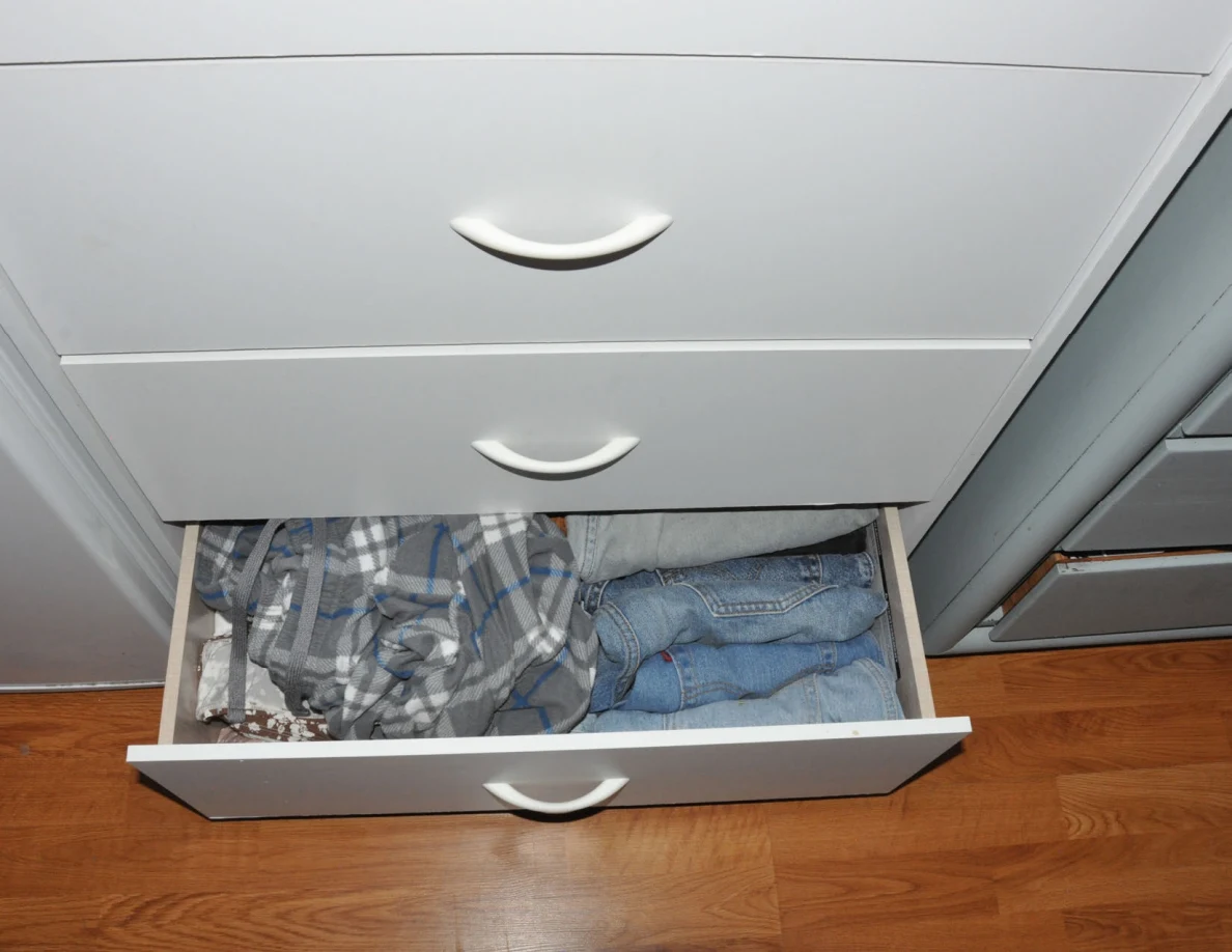 Open lower dresser drawer with plaid clothing and blue jeans.
