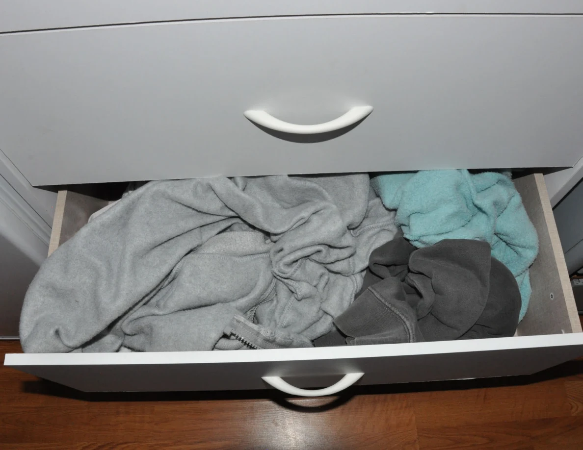 Open dresser drawer filled with gray, turquoise and dark clothing.