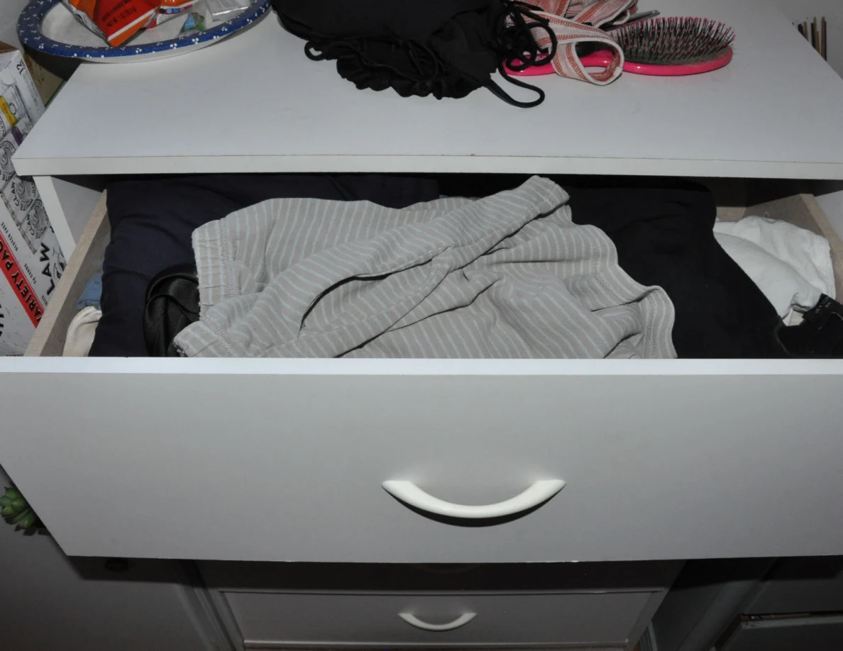 Upper dresser drawer with clothing below a top holding a hairbrush and accessories.
