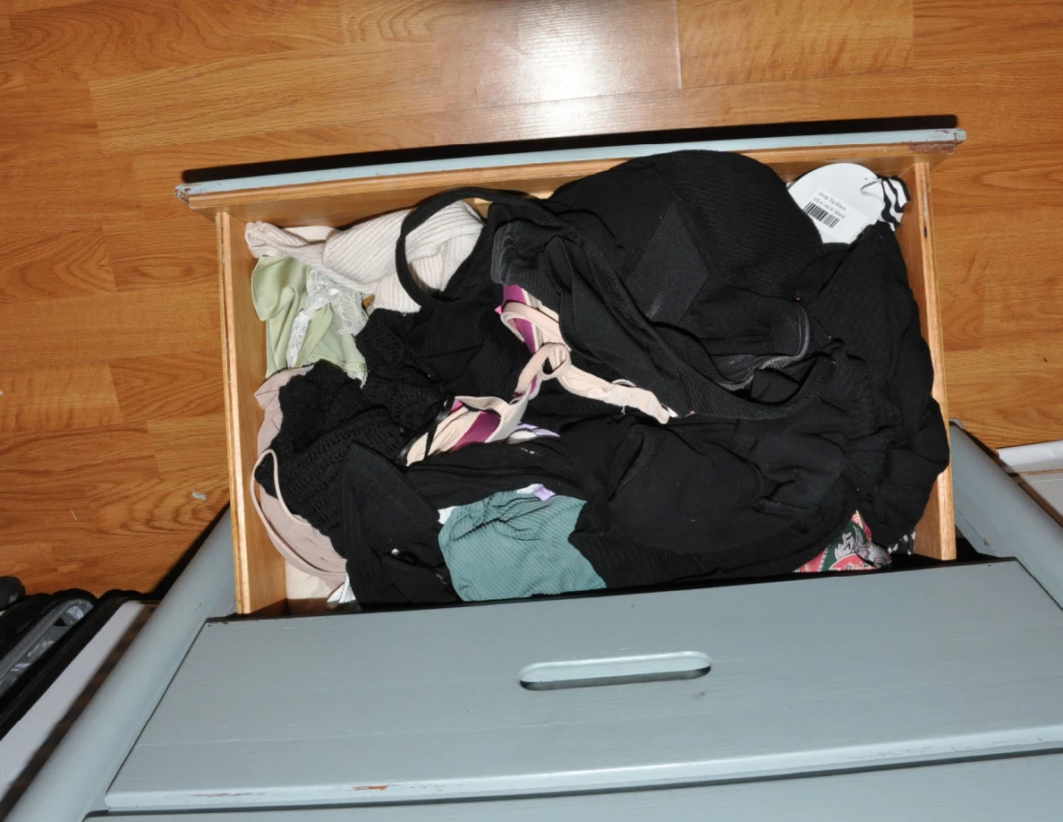 Open drawer containing mostly dark clothing and pale fabric.