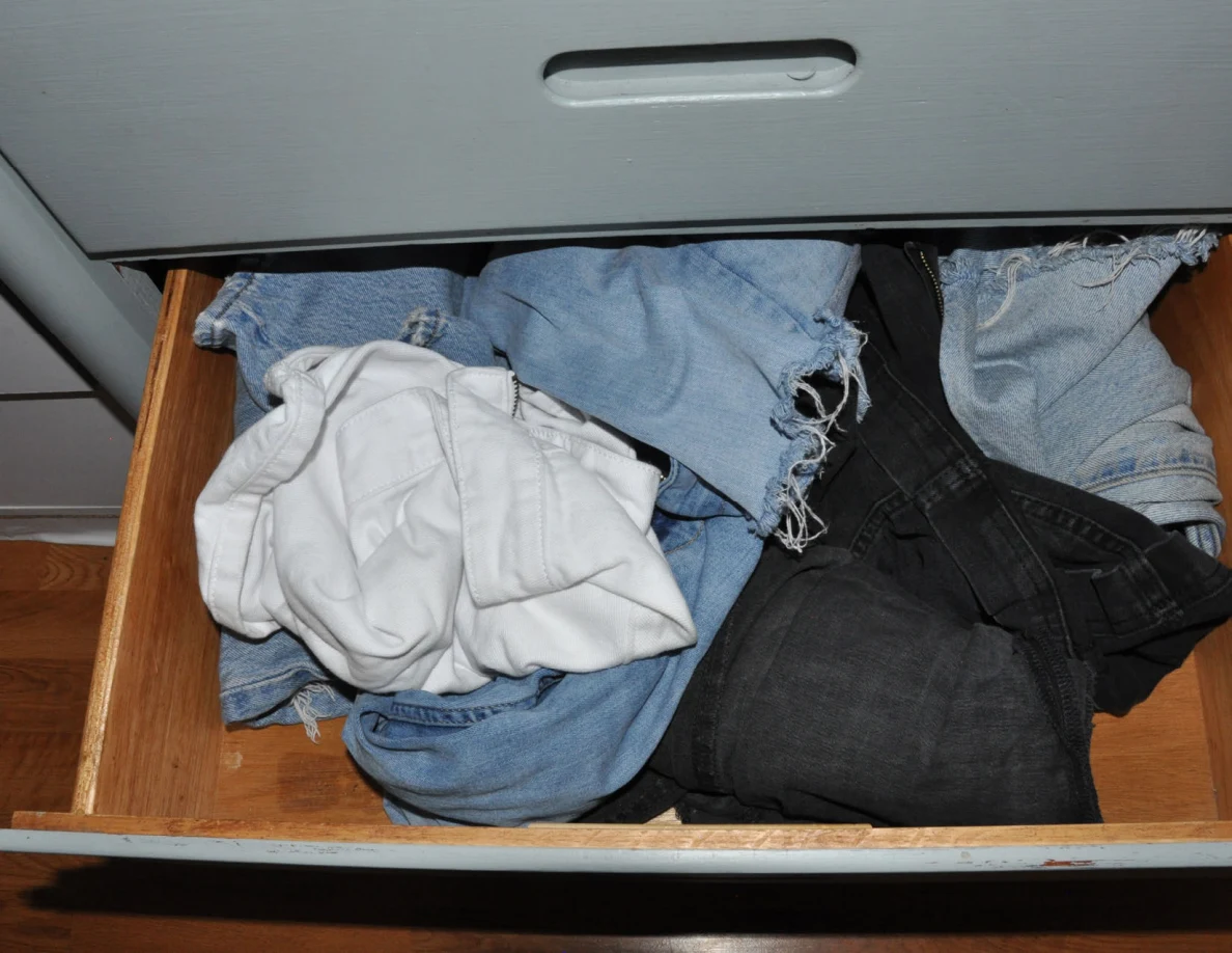 Open dresser drawer with denim shorts, jeans and a white garment.