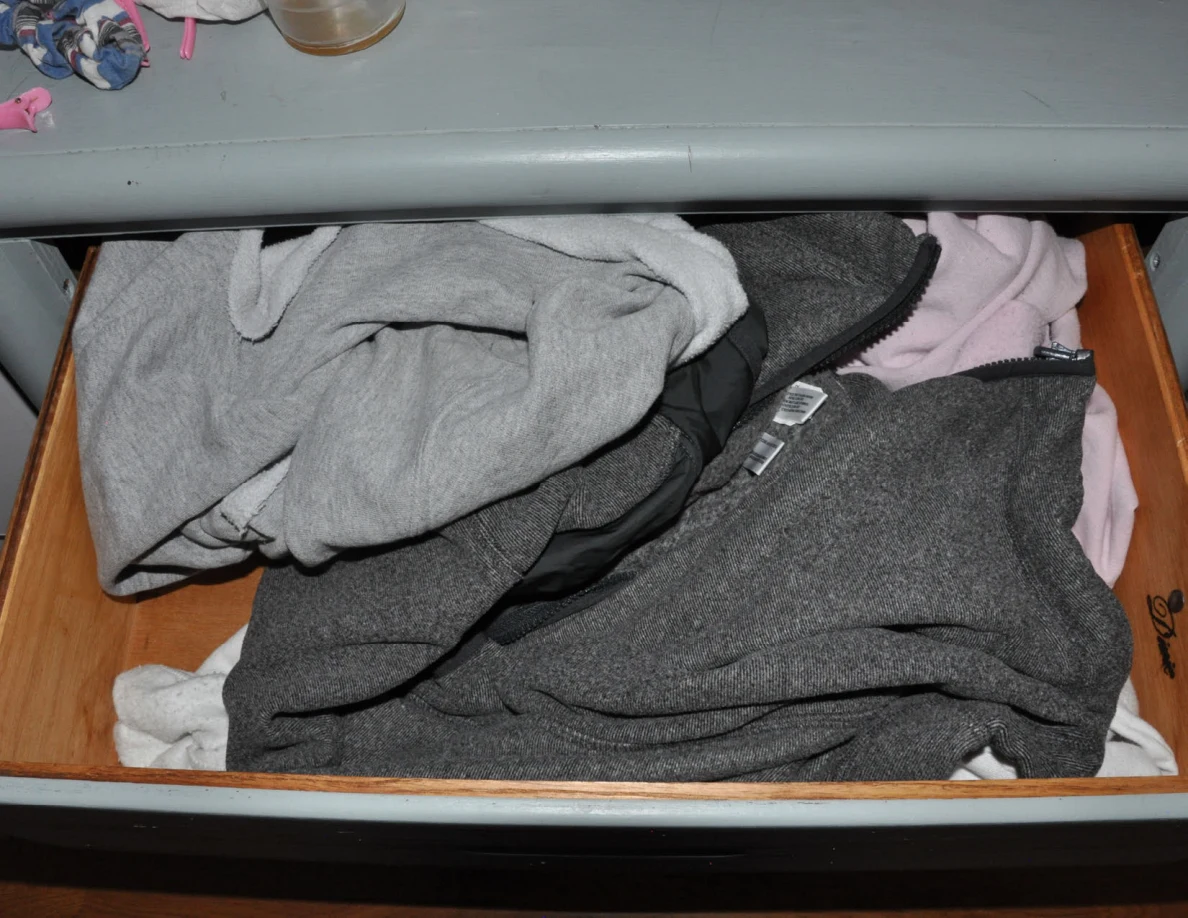 Open drawer filled with gray and pale clothing.