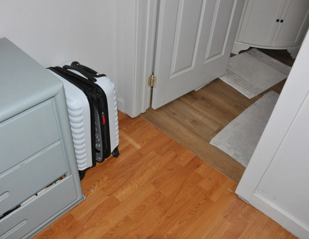 Suitcase beside a gray dresser near an open bathroom doorway and floor mats.