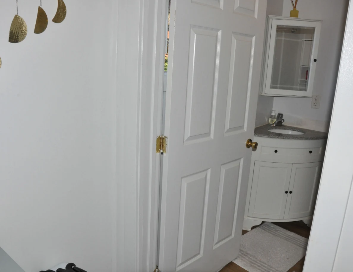 Open white bathroom door showing a curved vanity and mirrored cabinet.