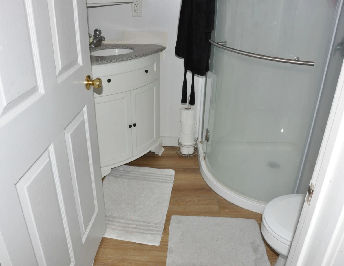 Compact bathroom with curved white vanity, glass shower and white toilet.