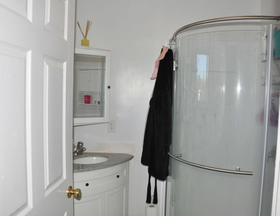 Glass shower enclosure beside a vanity mirror and hanging dark robe.