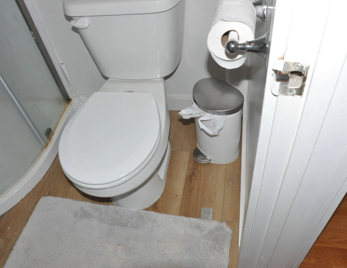 White toilet beside a small metal trash bin, toilet-paper roll and shower enclosure.