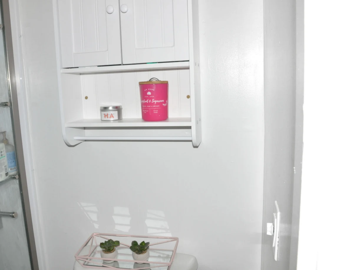 Wall cabinet above toilet with candles on an open shelf and small plants below.