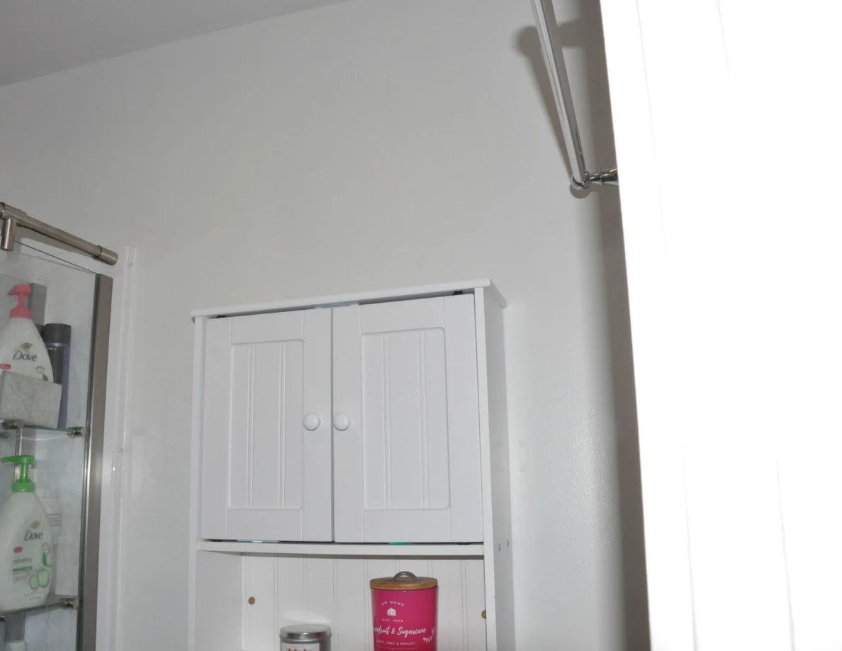 Upper bathroom wall cabinet beside shower shelves holding toiletries.