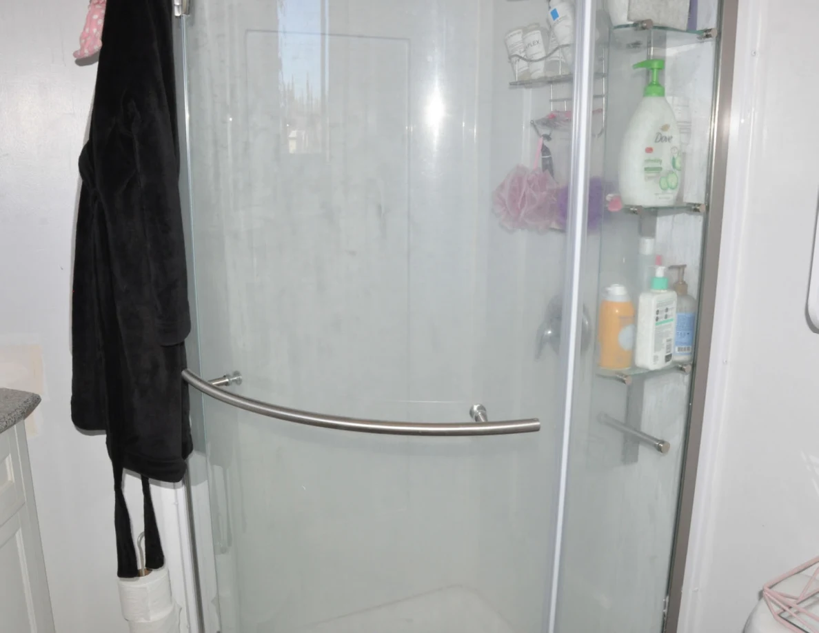 Glass shower door with metal handle, toiletry shelves and hanging robe.