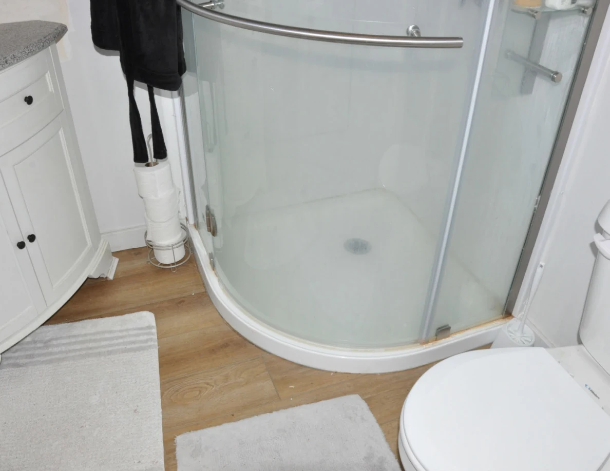 Shower base beside bathroom mats, vanity and partial toilet.