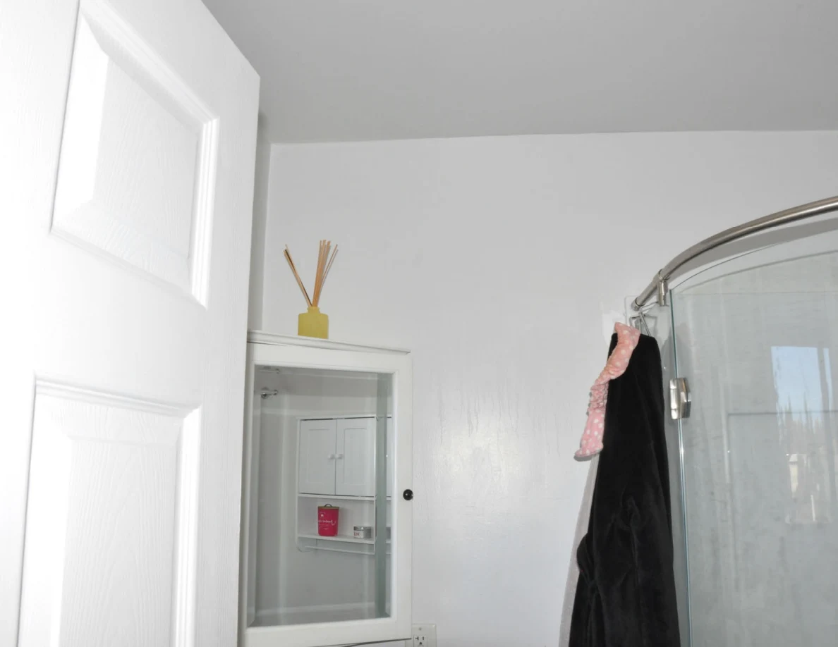 Upper bathroom door and wall beside mirror and curved shower rail.