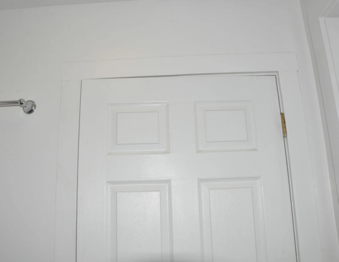 Upper white bathroom door and trim beside a metal towel bar.
