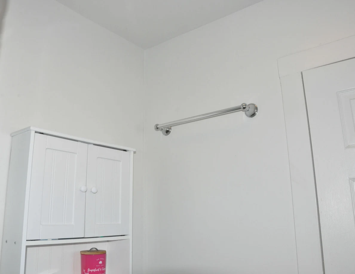 White wall cabinet and empty metal towel bar near bathroom door.