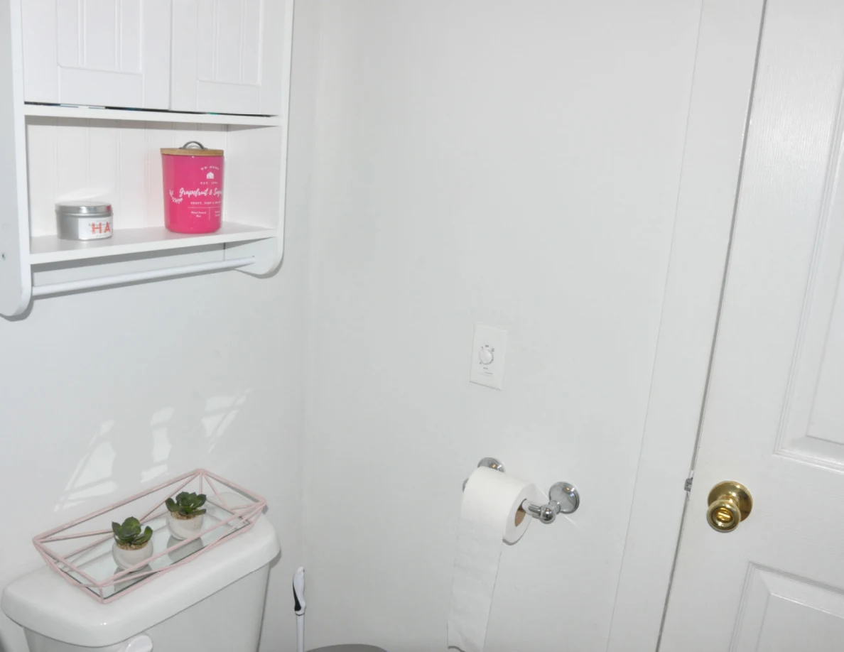 Toilet tank with small potted plants on a tray beneath a wall cabinet and candles.