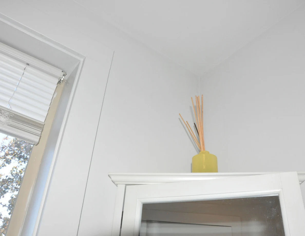 Yellow reed diffuser above a mirrored bathroom cabinet beside a window.