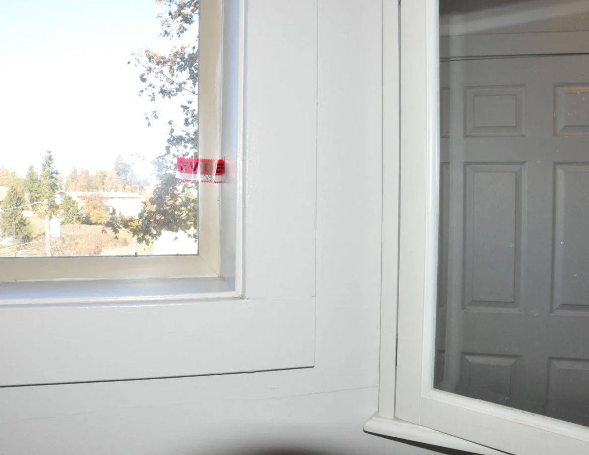 Bathroom window with red evidence tape on the frame beside a mirror reflecting a white door.