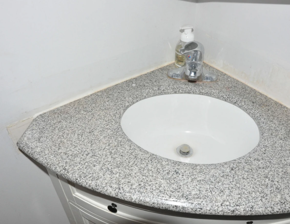 White oval bathroom sink in a rounded gray-speckled counter with chrome faucet and soap.