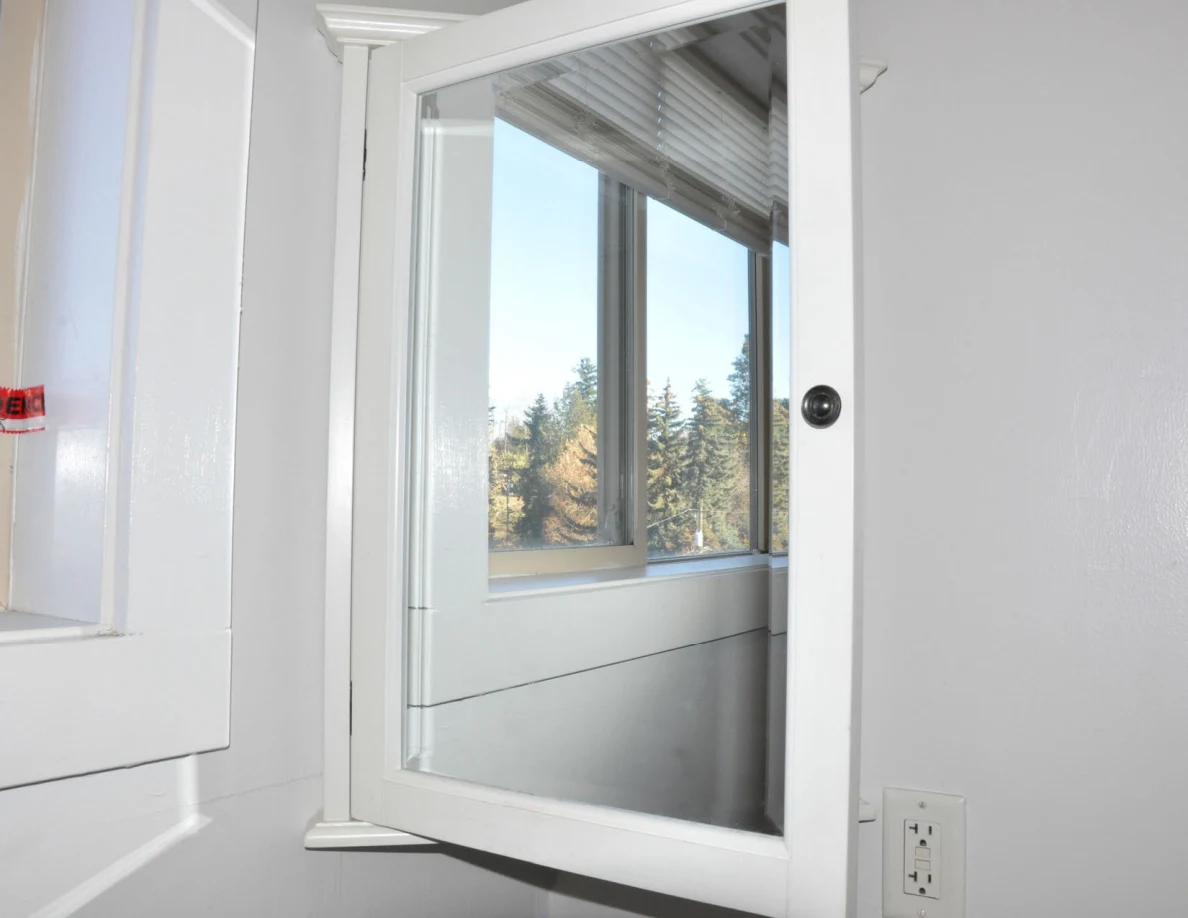 Mirrored bathroom cabinet door reflecting a window.