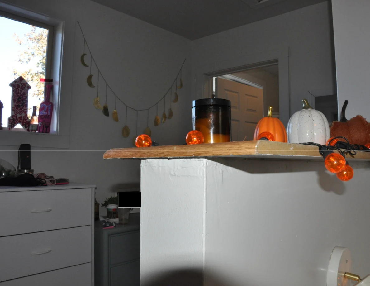 Stair landing half-wall with wood cap, decorative pumpkins, candles and orange string lights, with drawers and moon garland beyond.